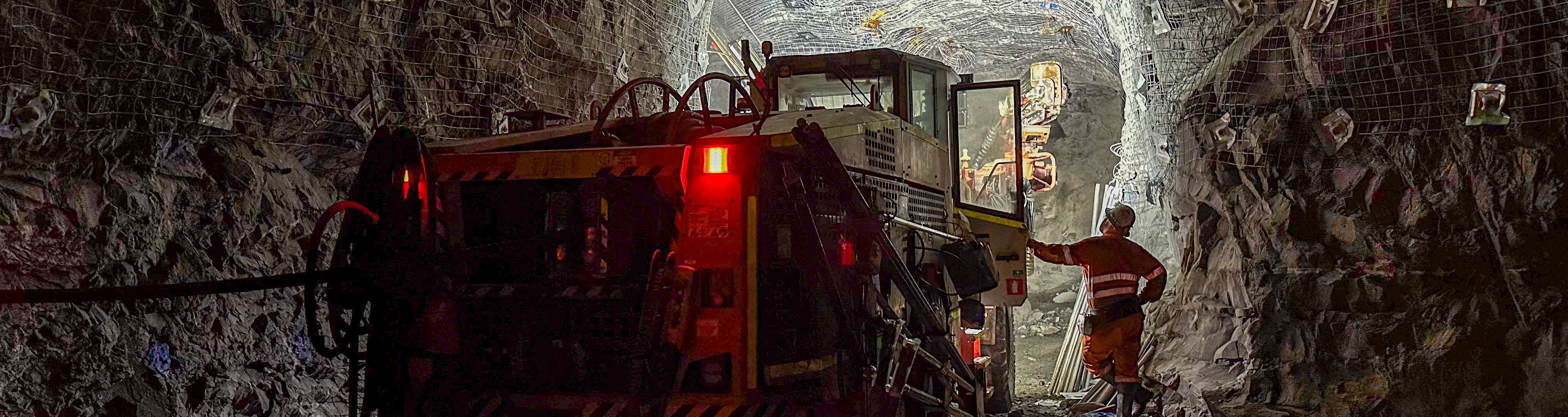 Heavy equipment operating underground with miner in PPE monitoring.